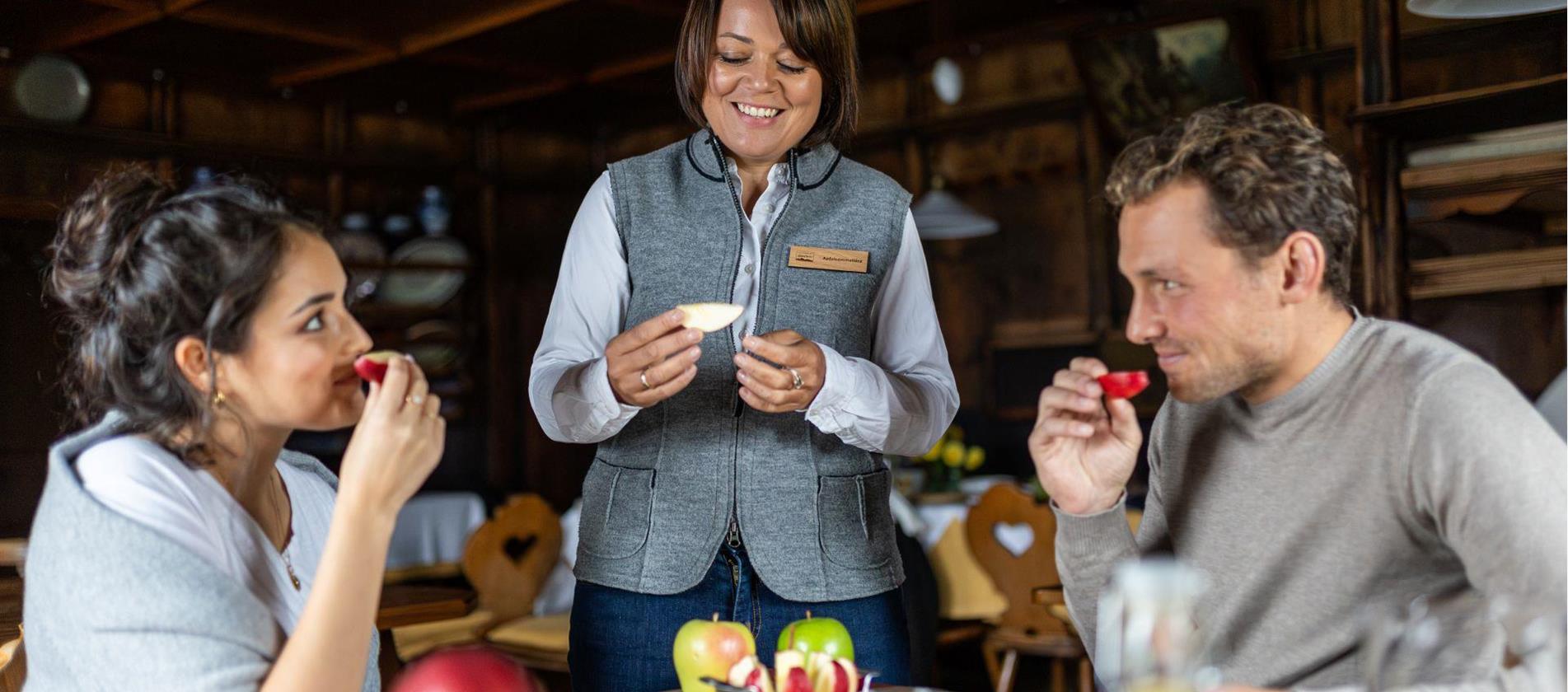 Zwei Personen verkosten Äpfel, eine Frau berät sie bei der Apfelverkostung