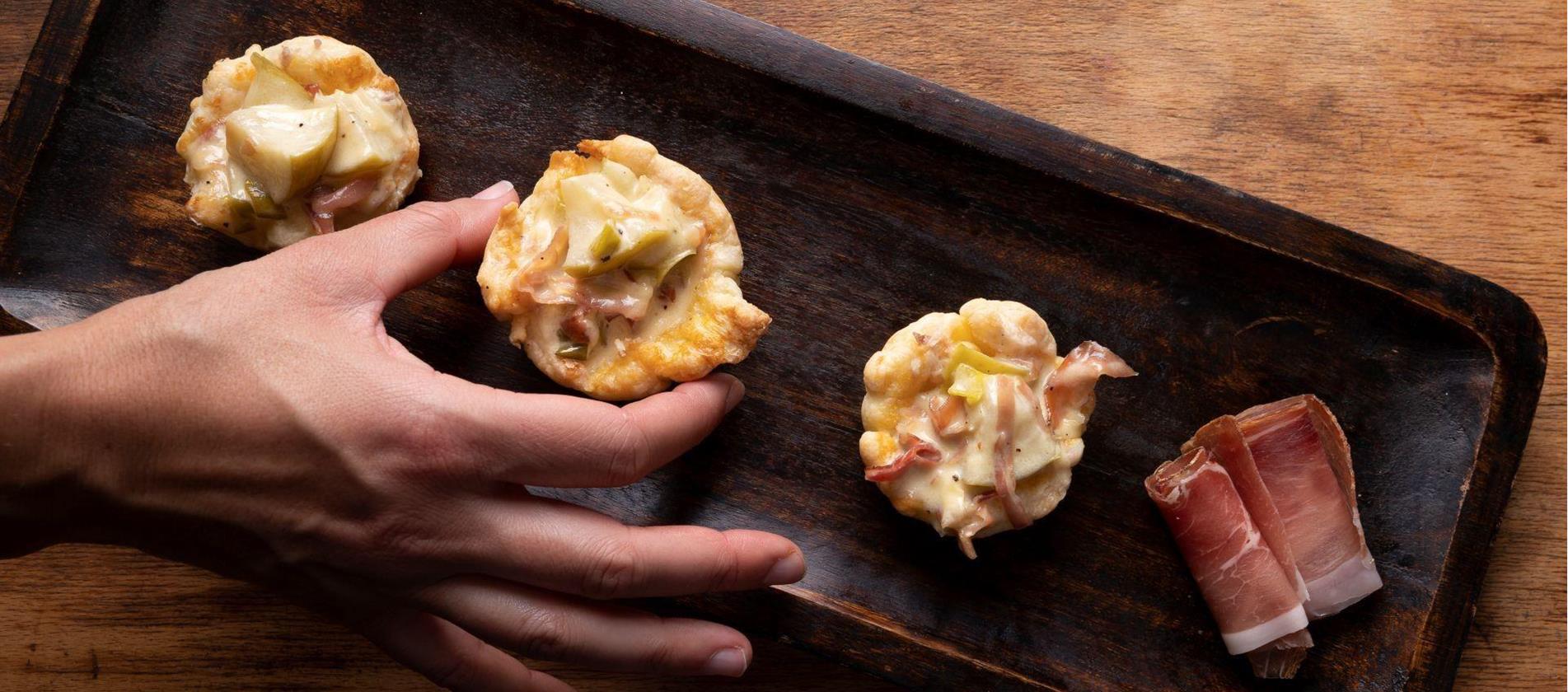 Blätterteig-Schiffchen mit Äpfeln und Speck auf einem dunklen Backblech.