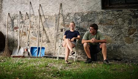 Andrea Erlacher und Jacob Gamper sitzen gemeinsam vor ihrem Hof neben verschiedenen Arbeitsgeräten.