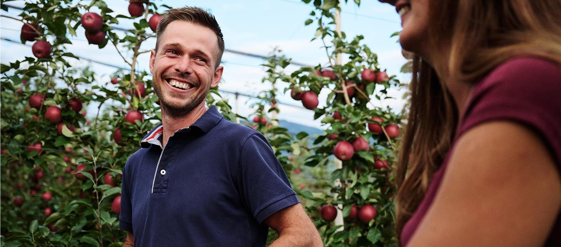 Zwei Personen lächeln sich an und stehen in Apfelwiesen mit reifen Äpfeln