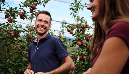 Zwei Personen lächeln sich an und stehen in Apfelwiesen mit reifen Äpfeln