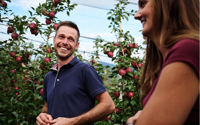 Zwei Personen lächeln sich an und stehen in Apfelwiesen mit reifen Äpfeln
