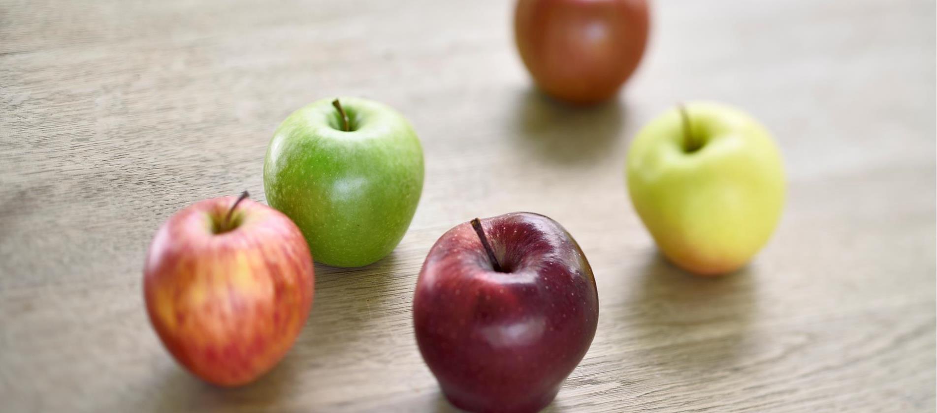 Südtiroler Äpfel in verschiedenen Farben, die auf einem Holztisch liegen.