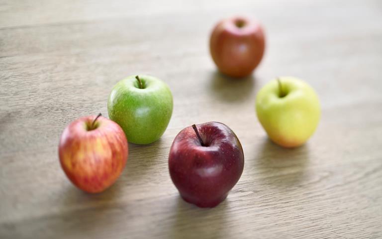 Südtiroler Äpfel in verschiedenen Farben, die auf einem Holztisch liegen.